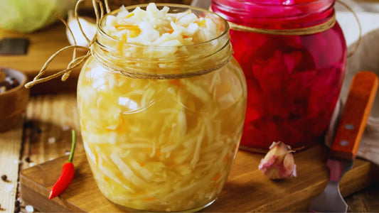 Glass jar of raw fermented cabbage with a red cabbage ferment in the background