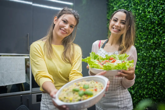 Two smiling women holding bowls of fresh vegetables and salad — healthy food choices that support gut health and mood