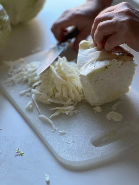 Hands shredding fresh cabbage with a knife to make homemade sauerkraut